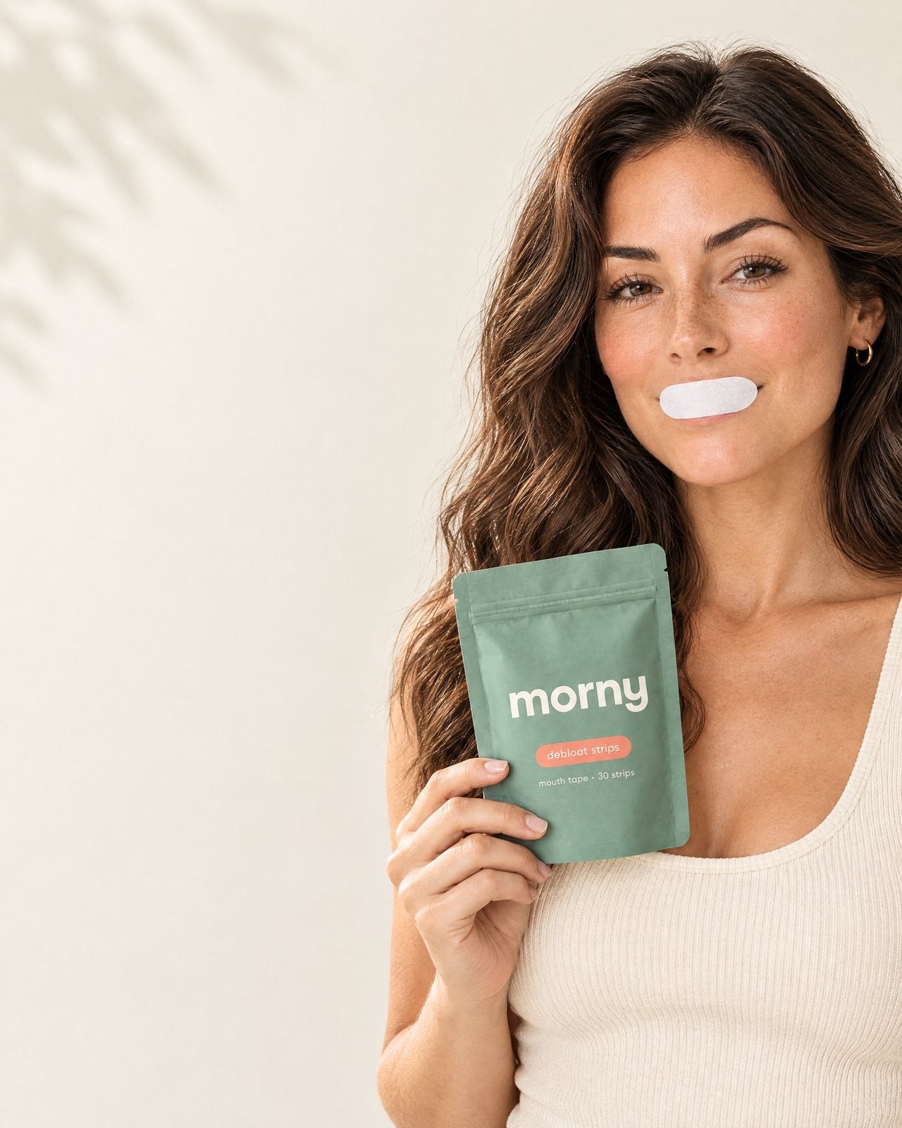 A woman wearing a morny strip over her lips, holding the morny debloat strips pouch